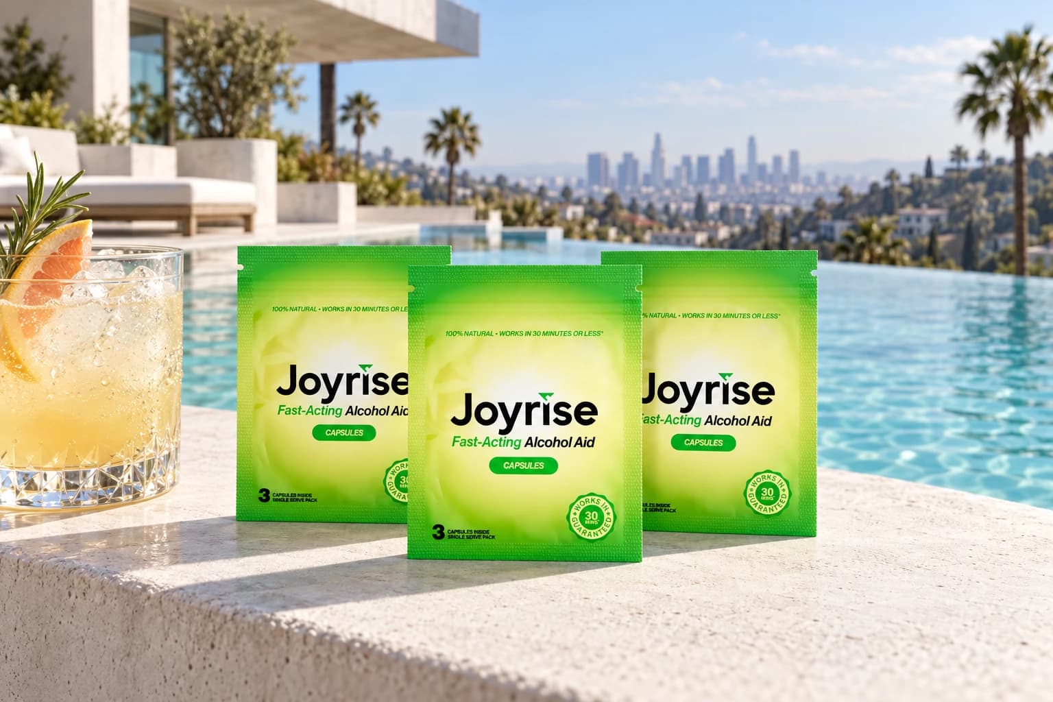 Three Joyrise capsule packets beside a citrus cocktail and infinity pool at a sunny white-concrete Hollywood Hills home